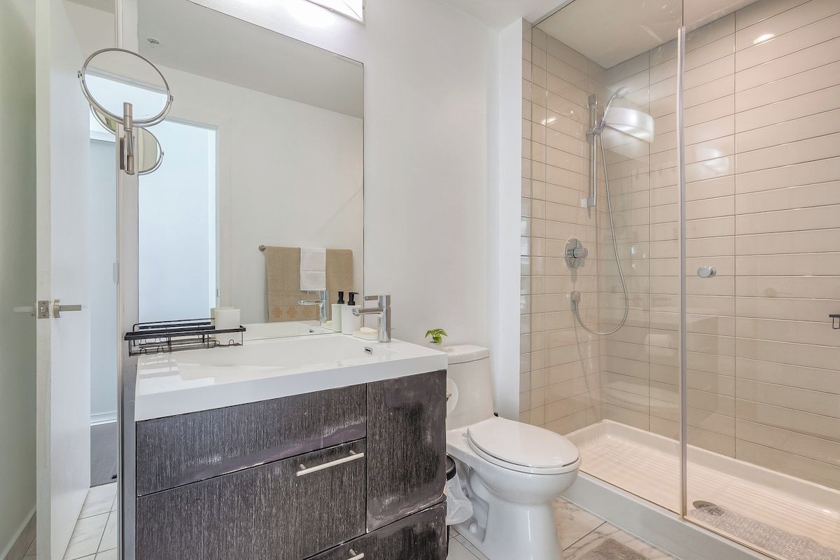 A modern bathroom with a glass-enclosed shower, a white toilet, and a vanity with a mirror.