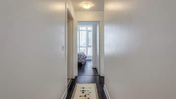 A narrow hallway with a patterned rug leading to a room with a bed and a window.