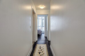 Passadís estret amb una catifes estampada que condueix a una habitació amb un llit i una finestra.