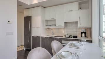 A modern kitchen with white cabinetry, a dining table set for two, and a view of the city through a large window.