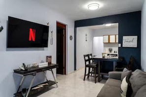 A living room with a TV, a dining area with chairs, a sofa, and a kitchen area with cabinets. - Charming 2BR in Aguada, PR, with AC Relax & Unwind (Aguada)