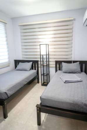 A bedroom with two beds, a wardrobe, and a window with blinds. - Charming 2BR in Aguada, PR, with AC Relax & Unwind (Aguada)