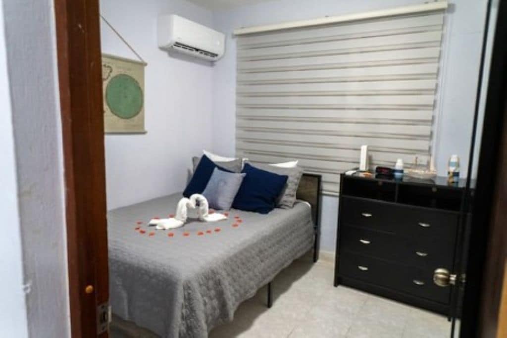 A bedroom with a bed, a dresser, a window with blinds, and an air conditioning unit.