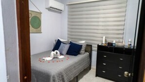 Ein Schlafzimmer mit einem Bett, einem Schminktisch, einem Fenster mit Jalousien und einer Klimaanlage.