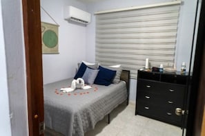 A bedroom with a bed, a dresser, a window with blinds, and an air conditioning unit. - Charming 2BR in Aguada, PR, with AC Relax & Unwind (Aguada)
