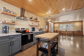 Eine moderne Küche mit Edelstahlgeräten, Holzregalen und einem Essbereich mit großem Tisch und Stühlen.