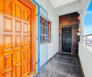 A hallway with a wooden door, a blue-framed window, and a black door with a metal grille. - Classic With Balcony Rama Home Stay (Tirupati)