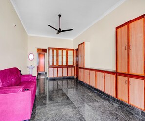 A room with a pink sofa, wooden cabinets, a ceiling fan, and a tiled floor. - Classic With Balcony Rama Home Stay (Tirupati)