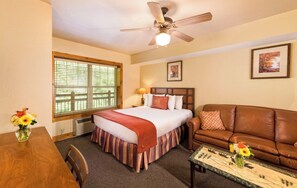 Ein Hotelzimmer mit einem Bett, einem braunen Ledersofa, einem Esstisch mit Stühlen und einem Deckenventilator.