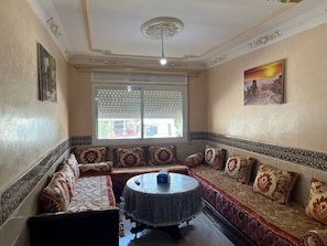 Una habitación con sofá, una mesa redonda y una ventana con persianas.