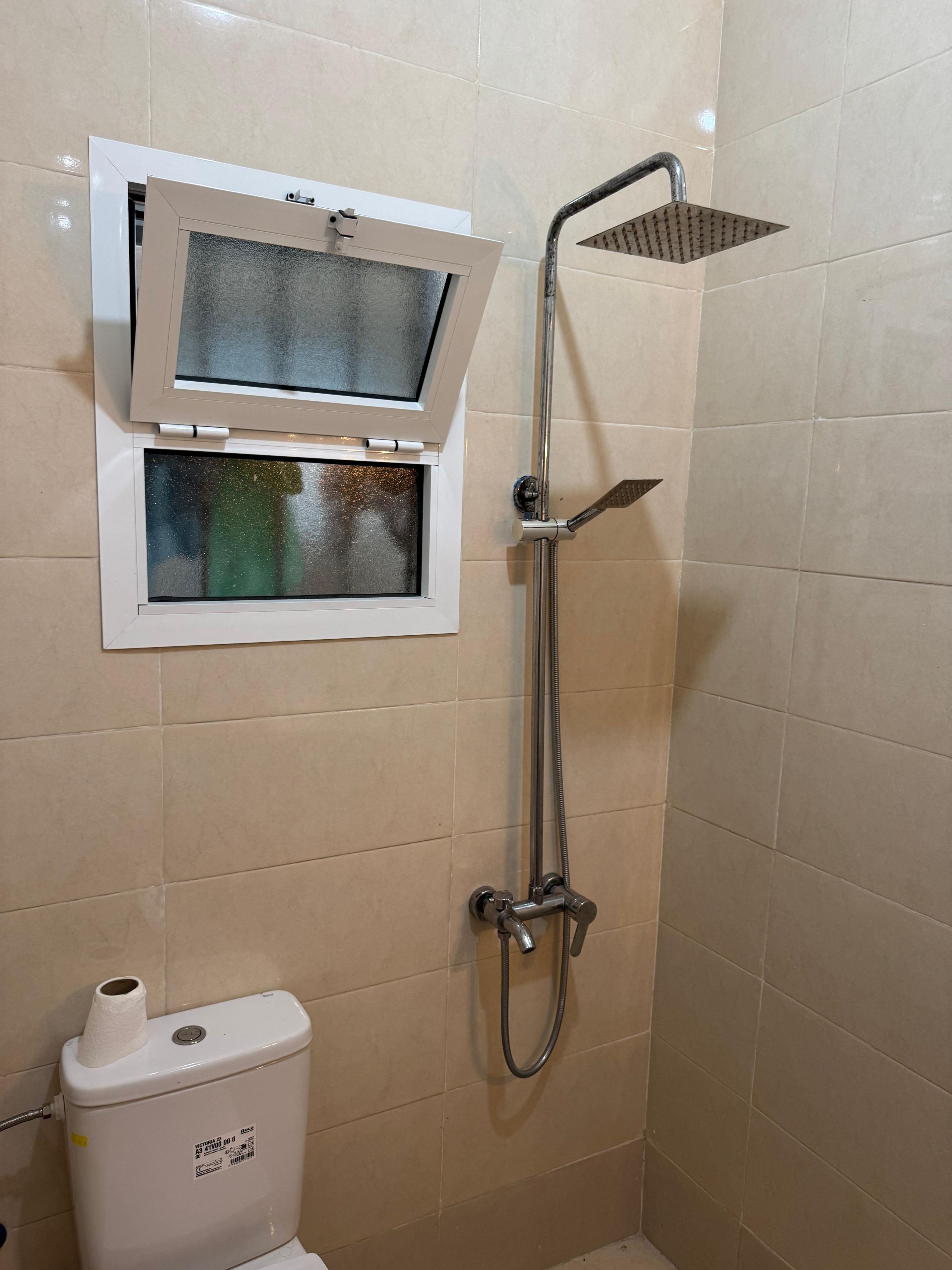 Un baño con ducha, inodoro y ventana con puerta de vidrio esmerilado.