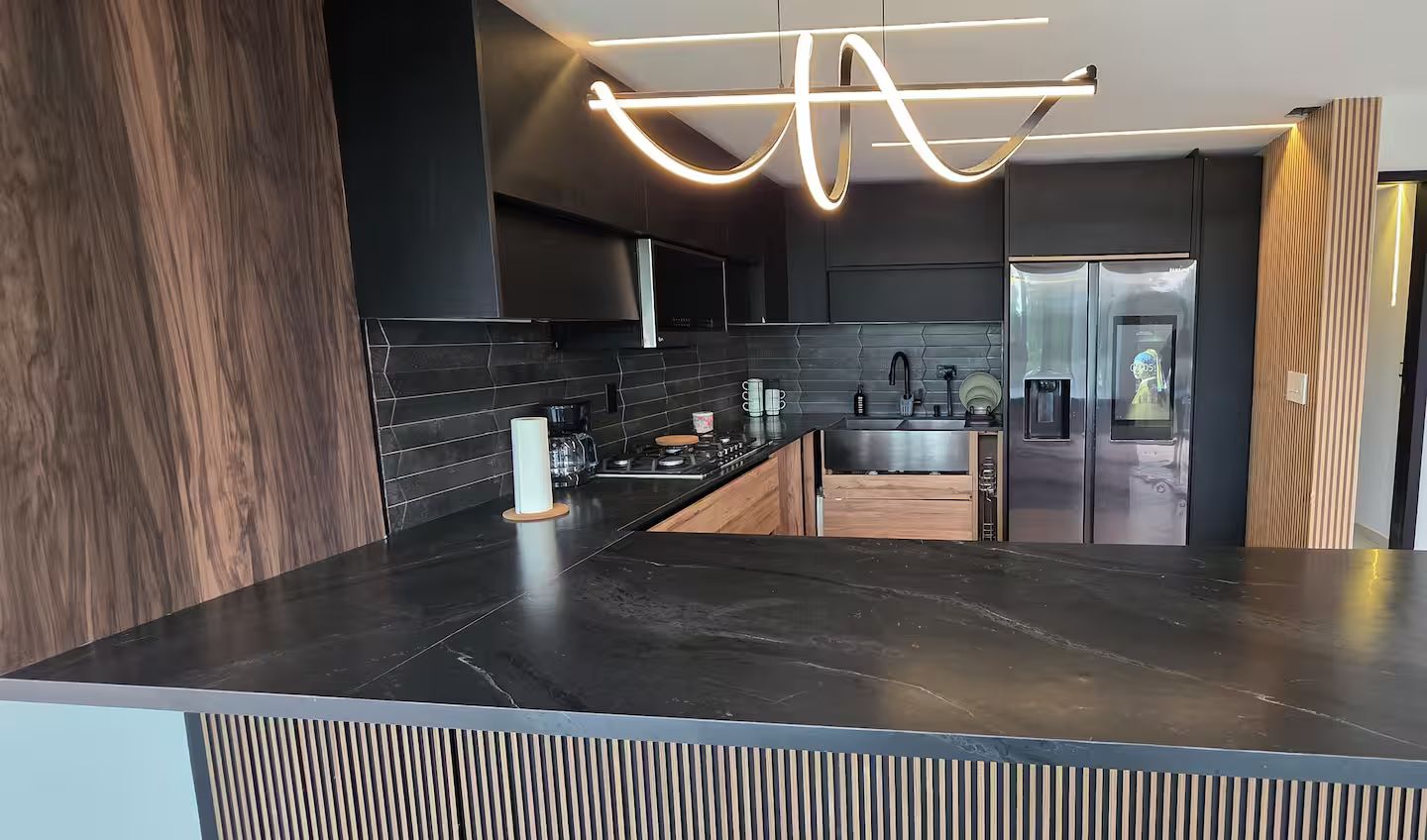 Una cocina moderna con encimera oscura, electrodomésticos de acero inoxidable y una lámpara de techo original.