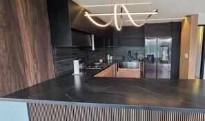 Una cocina moderna con encimera oscura, electrodomésticos de acero inoxidable y una lámpara de techo original.