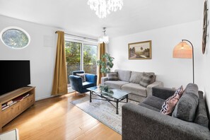 Una sala de estar moderna con televisor, sofá, sillón y una mesa de centro de vidrio.