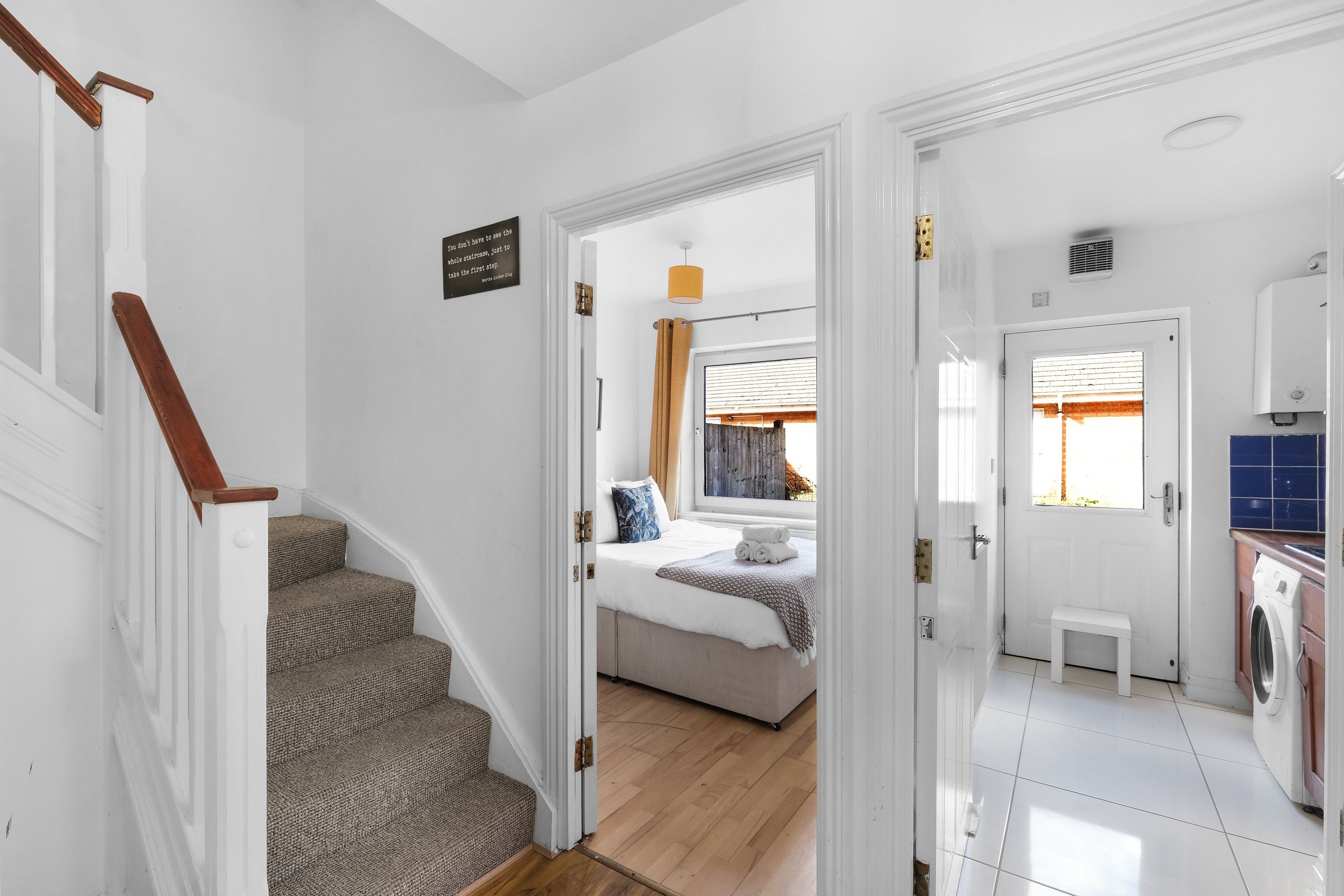 A staircase leading to a bedroom with a bed, a bathroom with a washing machine, and a kitchen area.