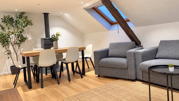 A modern loft with a dining area, a gray sofa, and a skylight. - book2stay: Apartment with 2 bedrooms, balcony near harbor & train station (Romanshorn)
