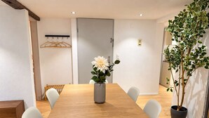 Une salle de conférence avec une longue table en bois, des chaises blanches, un vase avec des fleurs, un porte-manteau et une plante en pot.