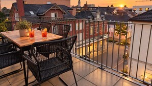A terrace with a table and chairs, overlooking a cityscape during sunset. - book2stay: Apartment with 2 bedrooms, balcony near harbor & train station (Romanshorn)