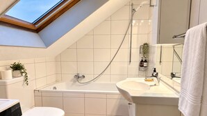 A modern bathroom with a skylight, a bathtub, a toilet, and a sink. - book2stay: Apartment with 2 bedrooms, balcony near harbor & train station (Romanshorn)