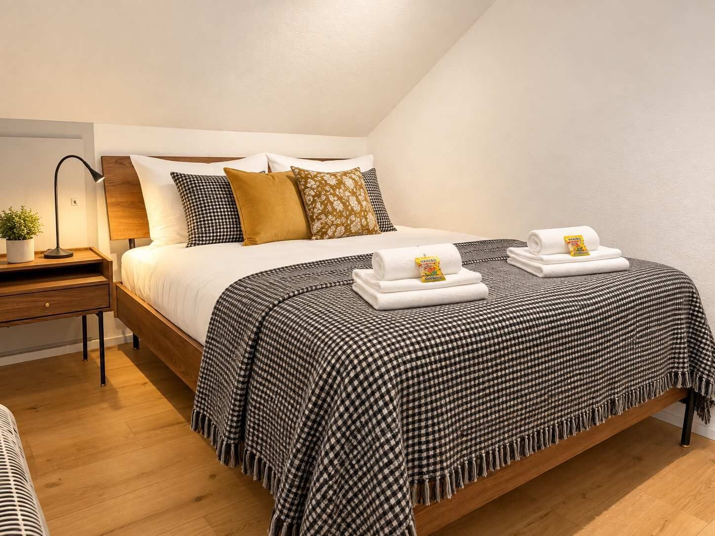 A neatly made bed with a checkered blanket, pillows, and rolled towels with a tag.