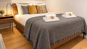 A neatly made bed with a checkered blanket, pillows, and rolled towels with a tag. - book2stay: Apartment with 2 bedrooms, balcony near harbor & train station (Romanshorn)