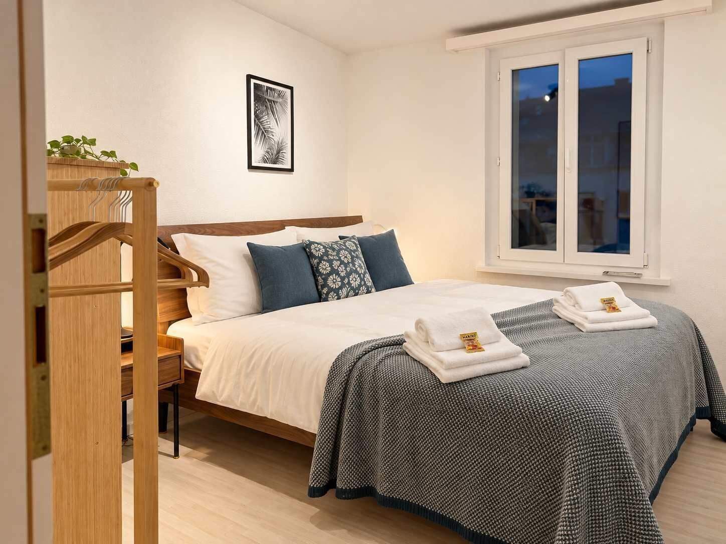 Un letto rifatto con cura, coperta fantasia, cuscini e un set di asciugamani.