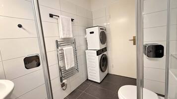 Une salle de bain moderne avec une douche à parois de verre, un lave-linge et un sèche-linge superposés, et des toilettes.