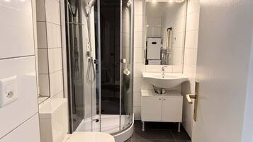 Une salle de bain moderne avec une douche à parois de verre, des toilettes blanches et un lavabo surmonté d’un miroir.