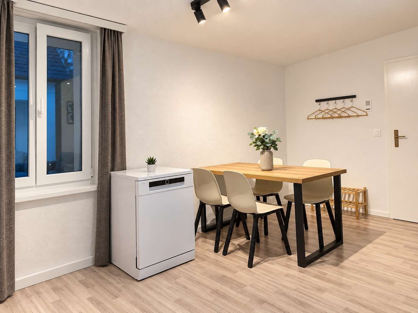 Ein gemütlicher Raum mit Esstisch, Stühlen, einem kleinen weißen Gerät und einem Fenster mit Vorhängen.