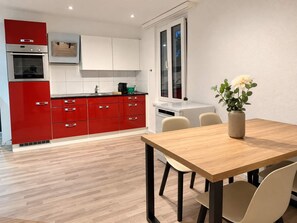 Una cucina moderna con mobili rossi, un forno integrato e una zona pranzo con tavolo e sedie in legno.