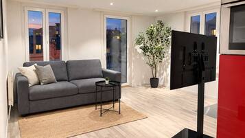 Un salon moderne avec un canapé gris, une petite table, une plante en pot et un téléviseur à écran plat.