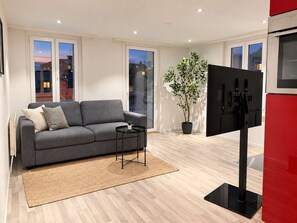 Un soggiorno moderno con un divano grigio, un tavolino, una pianta in vaso e una TV a schermo piatto.