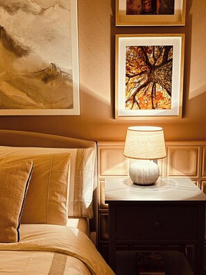 Ein Hotelzimmer mit einem Bett, einem Nachttisch mit Lampe und zwei gerahmten Kunstwerken an der Wand.