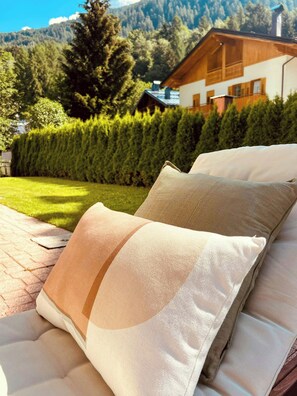 Ein Bett mit zwei Kissen und Blick auf ein Haus sowie Berge im Hintergrund.