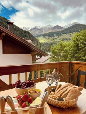A balcony with a table set for breakfast, overlooking a mountainous landscape. - Apartment with alpine views in Val di Pejo (Peio)