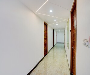 A hallway with white walls, wooden doors, and a marble floor. - Deluxe Govindpuri Station Formerly Montto Plaza (Kanpur)