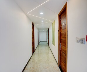 A hallway with a marble floor, wooden doors, and recessed ceiling lighting. - Deluxe Govindpuri Station Formerly Montto Plaza (Kanpur)