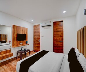 A hotel room with a bed, a TV mounted on the wall, a coffee table, and a wooden door. - Deluxe Govindpuri Station Formerly Montto Plaza (Kanpur)