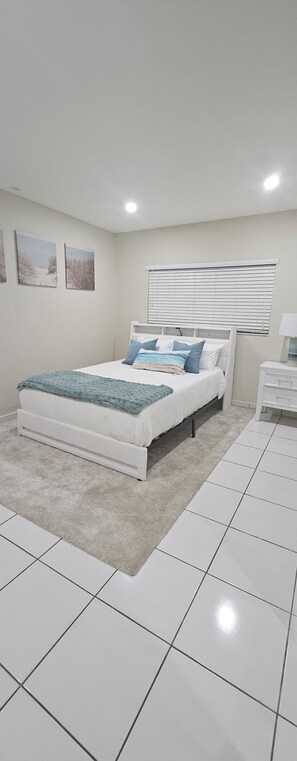 A bedroom with a bed, a bedside table, a nightstand, a window with blinds, and a wall with three framed pictures. - Gorgeous 1-bedroom house with AC in vibrant Miami,..free parking (Miami)