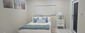 A bedroom with a bed, a bedside table with a lamp, a window with blinds, and a door. - Gorgeous 1-bedroom house with AC in vibrant Miami,..free parking (Miami)