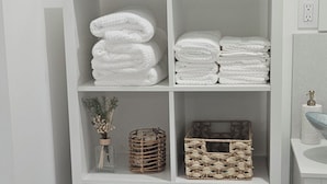 Une étagère blanche avec des serviettes pliées, des paniers en osier et une plante décorative.
