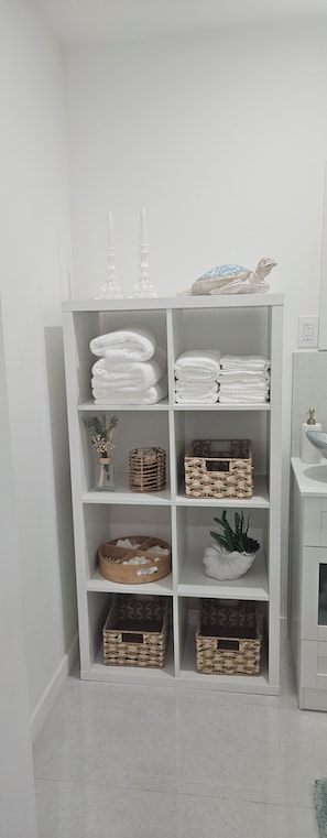 Uma estante branca com toalhas dobradas, cestos de vime e uma planta decorativa.