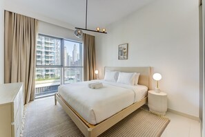 Ein Hotelzimmer mit einem großen Bett, einem Nachttisch, einer Lampe und Blick auf die Stadt.