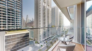 A high-rise building with a balcony featuring a glass railing, a wicker table with chairs, and a view of a cityscape with other buildings. - Elegant 1 Bed l Private Beach l Emaar Beachfront (Emaar Beachfront)