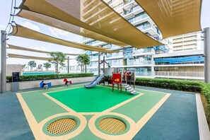 Ein Spielbereich im Freien mit Rutsche, Klettergerüsten und einem grünen, gummierten Untergrund.