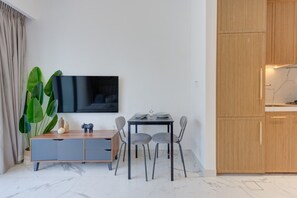Een moderne leefruimte met een flatscreen televisie aan de muur, een eettafel met vier stoelen, een houten kast en een grote groene plant.