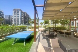 Een terras buiten met een tafeltennistafel, zitplaatsen en uitzicht op omliggende gebouwen.