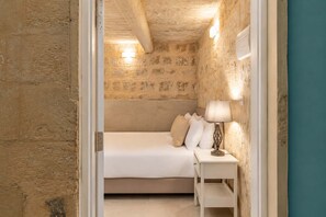 A bedroom with a stone wall, a bed with white bedding, and a bedside lamp. - Historic Valletta House, 3BR & Terrace (Valletta)