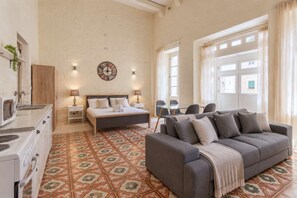 A spacious room with a bed, a sofa, a dining table, and a kitchen area. - Historic Valletta House, 3BR & Terrace (Valletta)