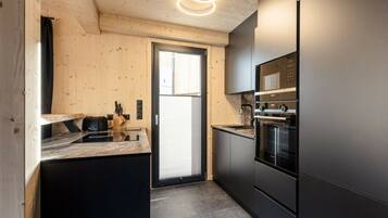 A modern kitchen with a black refrigerator, built-in oven, and a wooden ceiling.